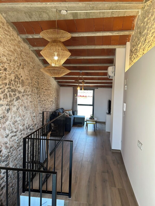 A spacious living area with a stone wall, wooden flooring, and a staircase with black railings. - We've just opened! New country house in Almatret, perfect for unwinding (Almatret)