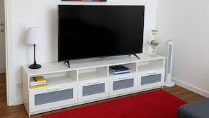 A modern living room with a flat-screen TV on a white entertainment unit, a red rug, and a colorful abstract painting above the TV. - Detached house in the center of Tonfano • 100 m from the sea • 2 parking spaces (Marina di Pietrasanta)
