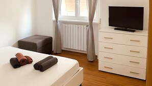 A bedroom with a bed, a TV on a dresser, a radiator, and a window with curtains. - Detached house in the center of Tonfano • 100 m from the sea • 2 parking spaces (Marina di Pietrasanta)