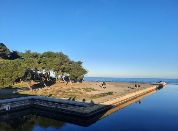 A calm beach with a clear sky, a calm sea, and a few people walking along the shore.