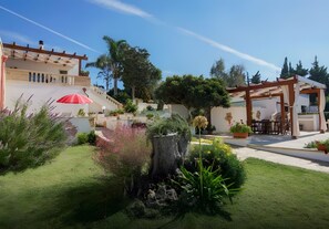 A garden with a pergola, a red umbrella, and a stone wall.