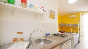Una cocina con un lavamanos, estufa y una cama litera al fondo.