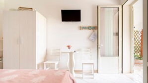 A bedroom with a bed, a TV, a small table with chairs, and a door leading to a balcony. - Room 'Arancio' with Lake View, Wi-Fi and Air Conditioning (Otranto)