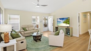 A spacious living room with a flat-screen TV, beige sofas, a coffee table, and a ceiling fan. - ☀️Private Pool | Pet Friendly | Close to Beach | Citrus Sol☀️ (Fort Myers Beach)