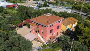 Um edifício de vários andares com telhado vermelho, rodeado por vegetação e um caminho de paralelepípedos.