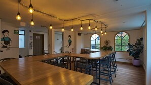Un vaste espace dédié à la salle à manger, avec une longue table en bois, de nombreuses chaises et des luminaires suspendus.