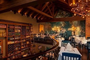 A restaurant with a wine cellar, a mural, and a dining area with tables and chairs.