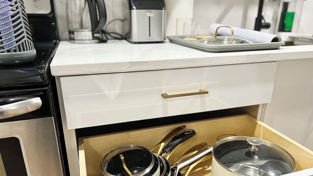 Una cocina con mostrador blanco, un tostador, una tetera y un cajón con ollas y sartenes.