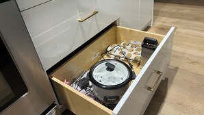 Un cajón de cocina con una olla de cocción lenta, una regleta de enchufes y un cargador portátil.