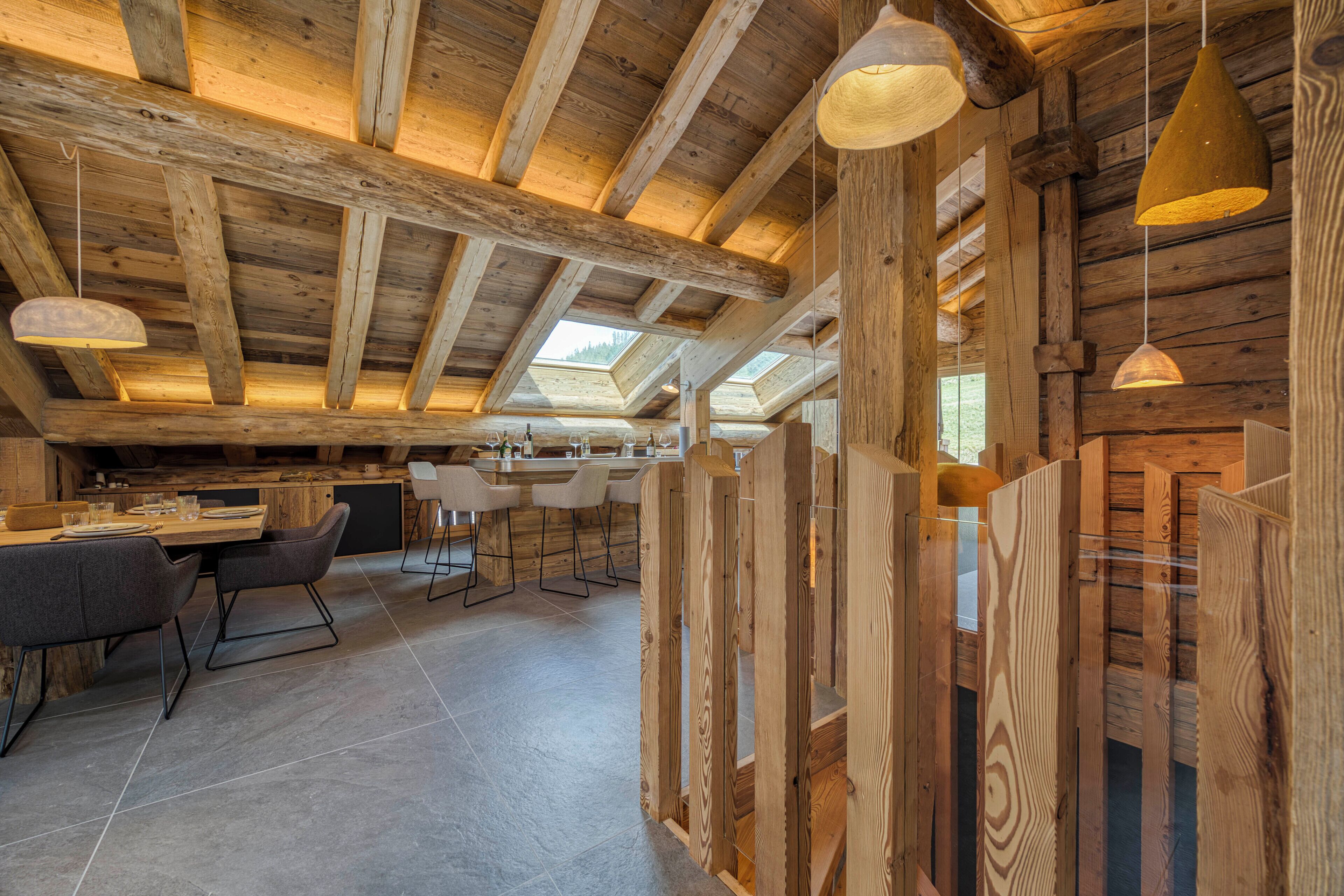 A rustic wooden interior with a high ceiling, exposed beams, and a dining area with modern chairs and a table.