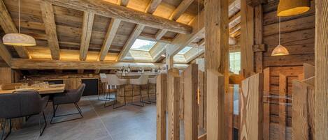A rustic wooden interior with a high ceiling, exposed beams, and a dining area with modern chairs and a table.
