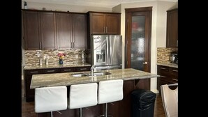 A modern kitchen with dark wood cabinets, a stainless steel refrigerator, and a granite countertop. - Spacious 4BR Retreat- Perfect for Families & Groups! (Airdrie)