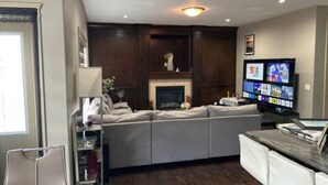 A modern living room with a large sectional sofa, a fireplace, a flat-screen TV, and a bar area. - Spacious 4BR Retreat- Perfect for Families & Groups! (Airdrie)