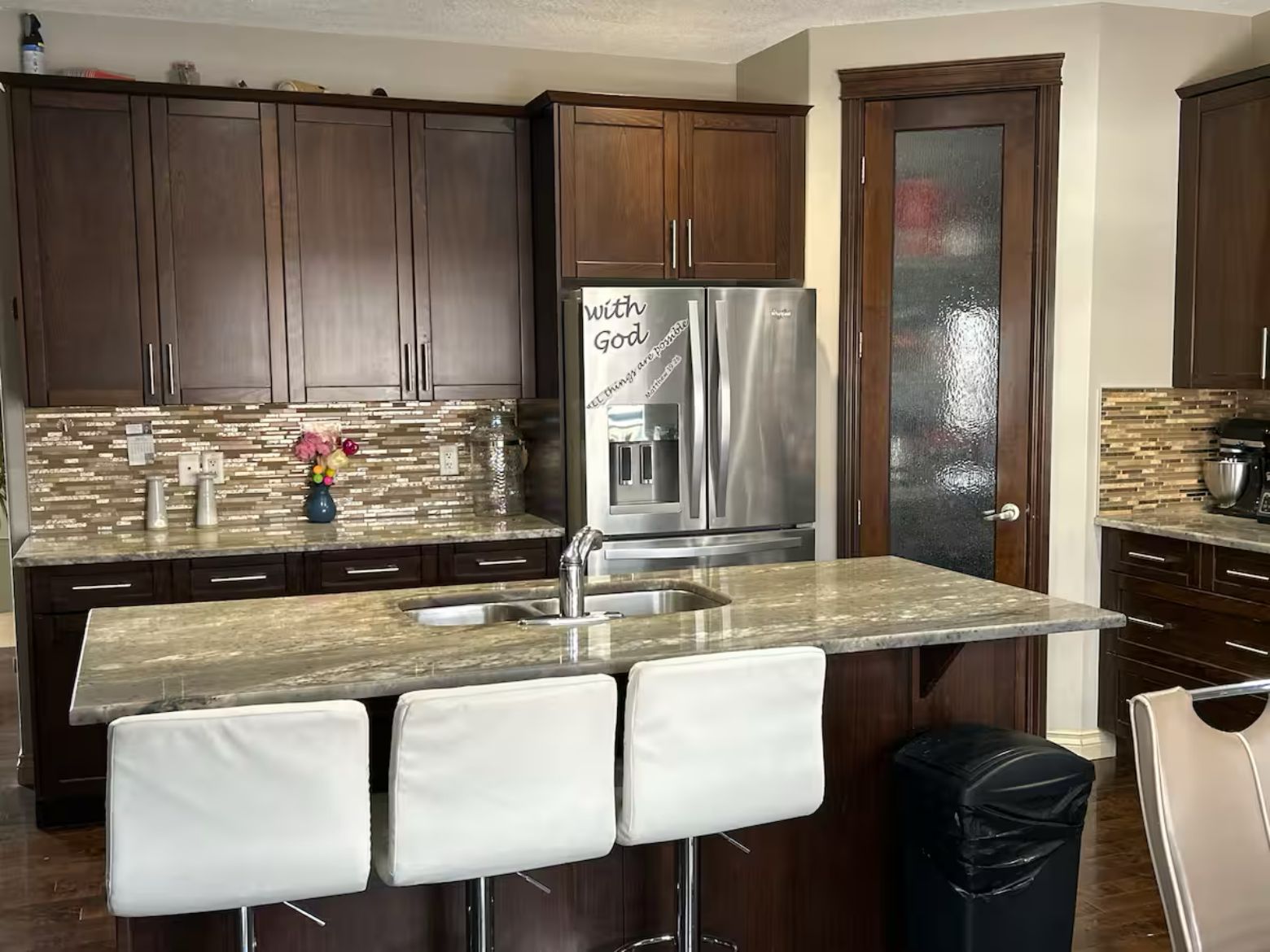 A modern kitchen with dark wood cabinets, a stainless steel refrigerator, and a granite countertop.