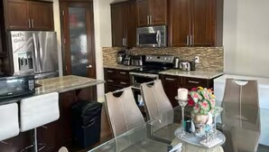 A modern kitchen with dark wooden cabinets, stainless steel appliances, and a glass dining table with chairs. - Spacious 4BR Retreat- Perfect for Families & Groups! (Airdrie)