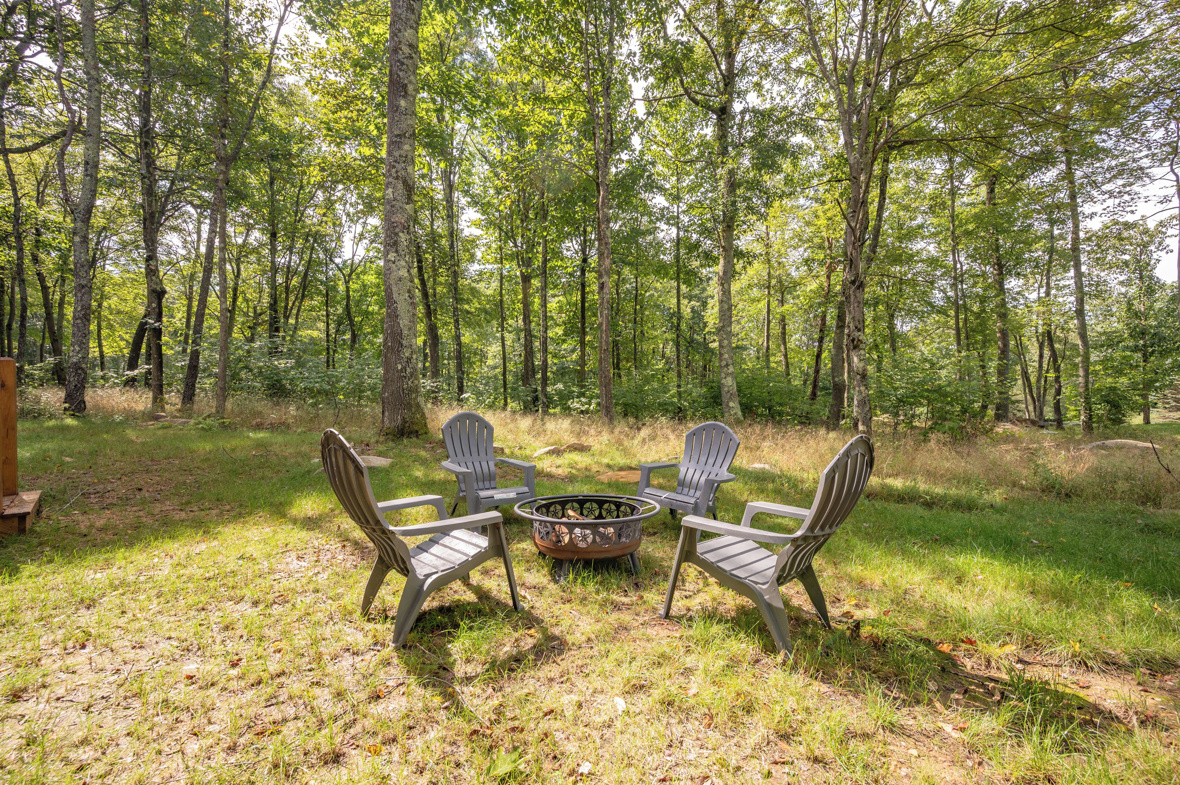An outdoor seating area with Adirondack chairs and a fire pit surrounded by a forest.