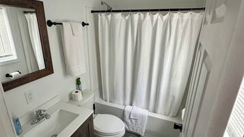Een badkamer met een wit wastafelmeubel, toilet, bad en douchegordijn.