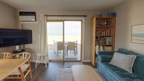 Uma sala de estar com televisão, sofá, estante e porta de vidro correr que dá para área externa.