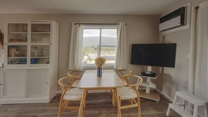 Uma área de refeições com uma mesa e cadeiras de madeira, um armário com portas de vidro, uma televisão e uma janela com cortinas.