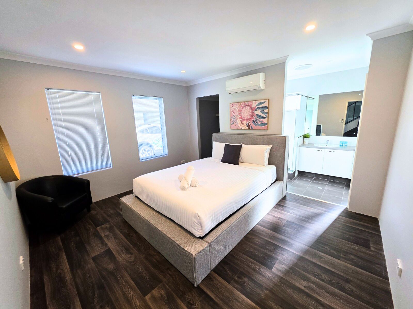 A modern bedroom with a large bed, a chair, and a bathroom visible in the background.
