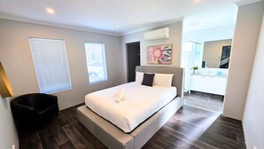 Ett modernt sovrum med en stor säng, en stol och ett badrum som syns i bakgrunden.