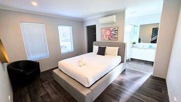 A modern bedroom with a large bed, a chair, and a bathroom visible in the background.