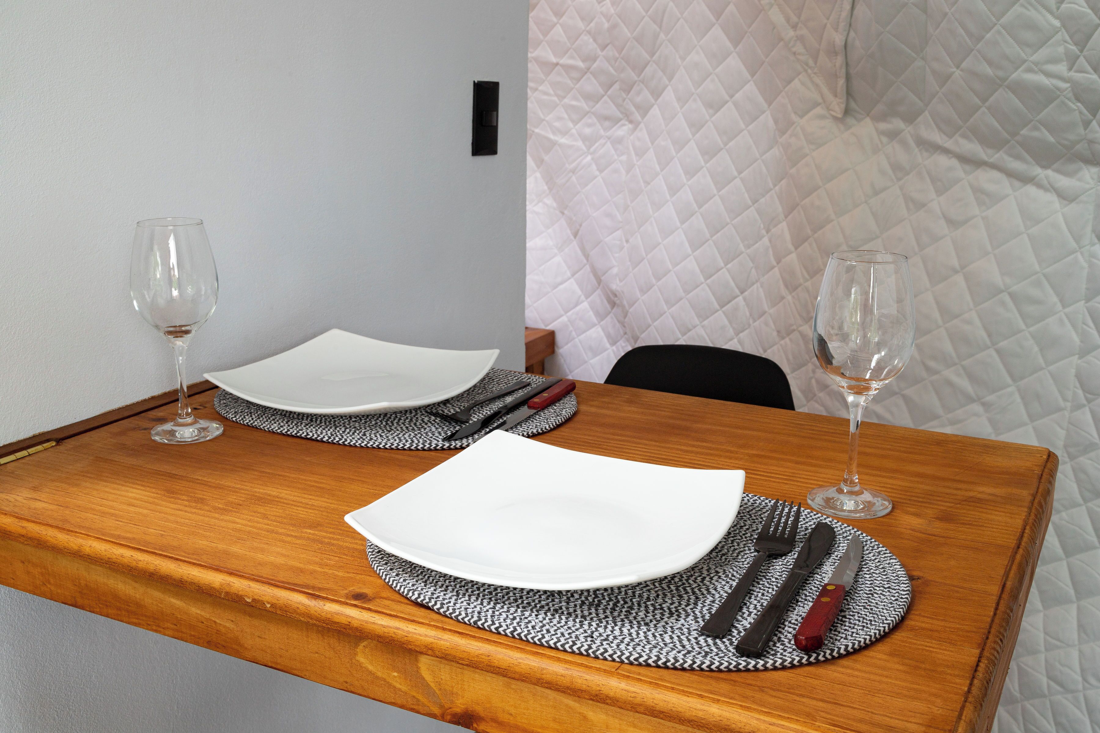 A dining table with two plates, cutlery, and wine glasses set for two.