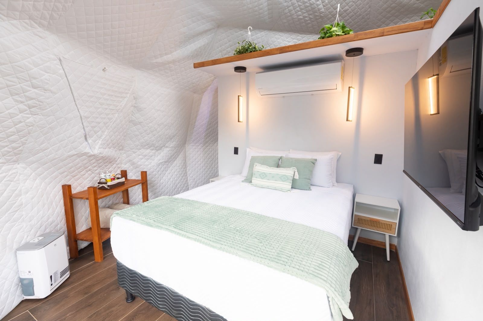 Une chambre à coucher moderne et compacte, comprenant un lit, des tables de chevet, un petit coin salon et un téléviseur fixé au mur.