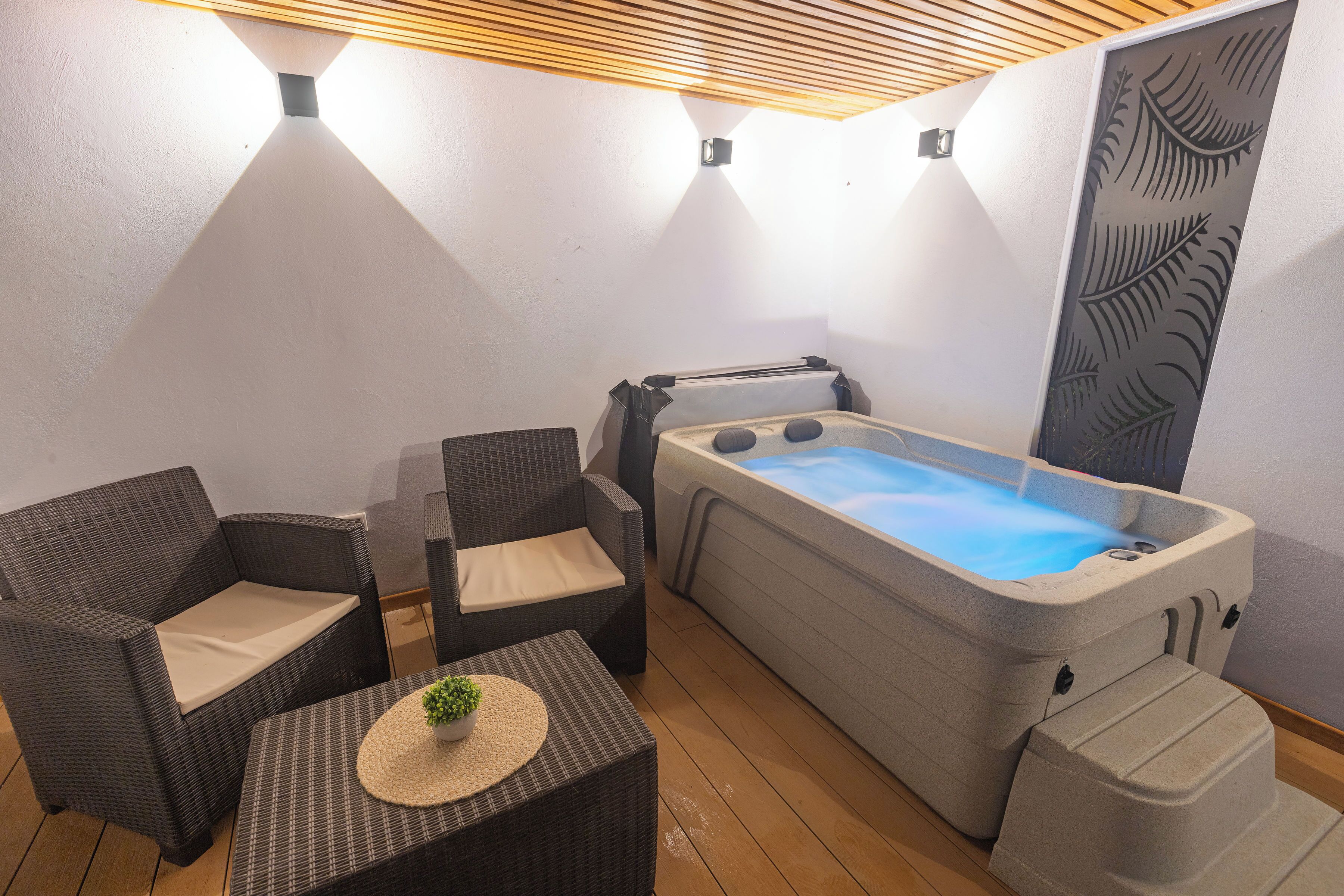 Un espace détente avec un jacuzzi, des fauteuils en osier et une petite table agrémentée d’une plante.