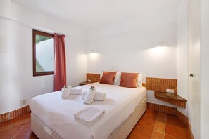 A hotel room with a bed, a nightstand, a window with curtains, and a wall-mounted shelf.