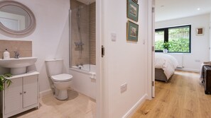 Une salle de bain moderne avec un lavabo, des toilettes et une douche. On y trouve un meuble en bois et un miroir au-dessus du lavabo. La pièce est dotée d’un plancher en bois et d’une fenêtre donnant sur un paysage verdoyant.