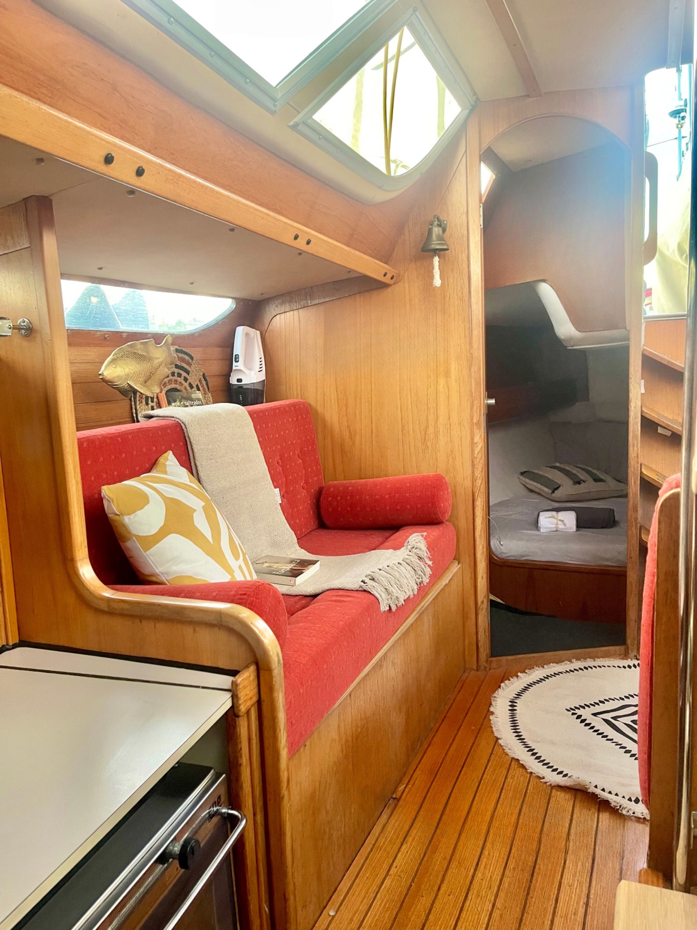 Un intérieur compact en bois, avec un banc rembourré de couleur rouge, une petite table et un lit compact.