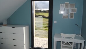 A room with a white dresser, a desk with a chair, a door leading to a balcony, and wall-mounted light switches. - Gîte 'Des Taravelles' with Private Pool, Private Terrace and Wi-Fi (Manzat)