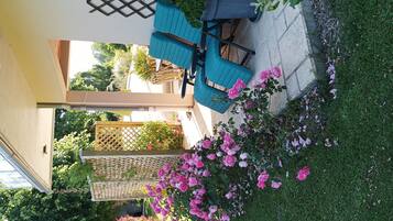 Un espace patio aménagé avec une table et des chaises, une pergola en bois et un jardin agrémenté de fleurs roses.