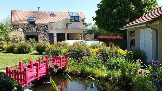 A house with a stone facade, a red-tiled roof, and a small garden with a pink bridge over a pond. - Gîte 'Des Taravelles' with Private Pool, Private Terrace and Wi-Fi (Manzat)
