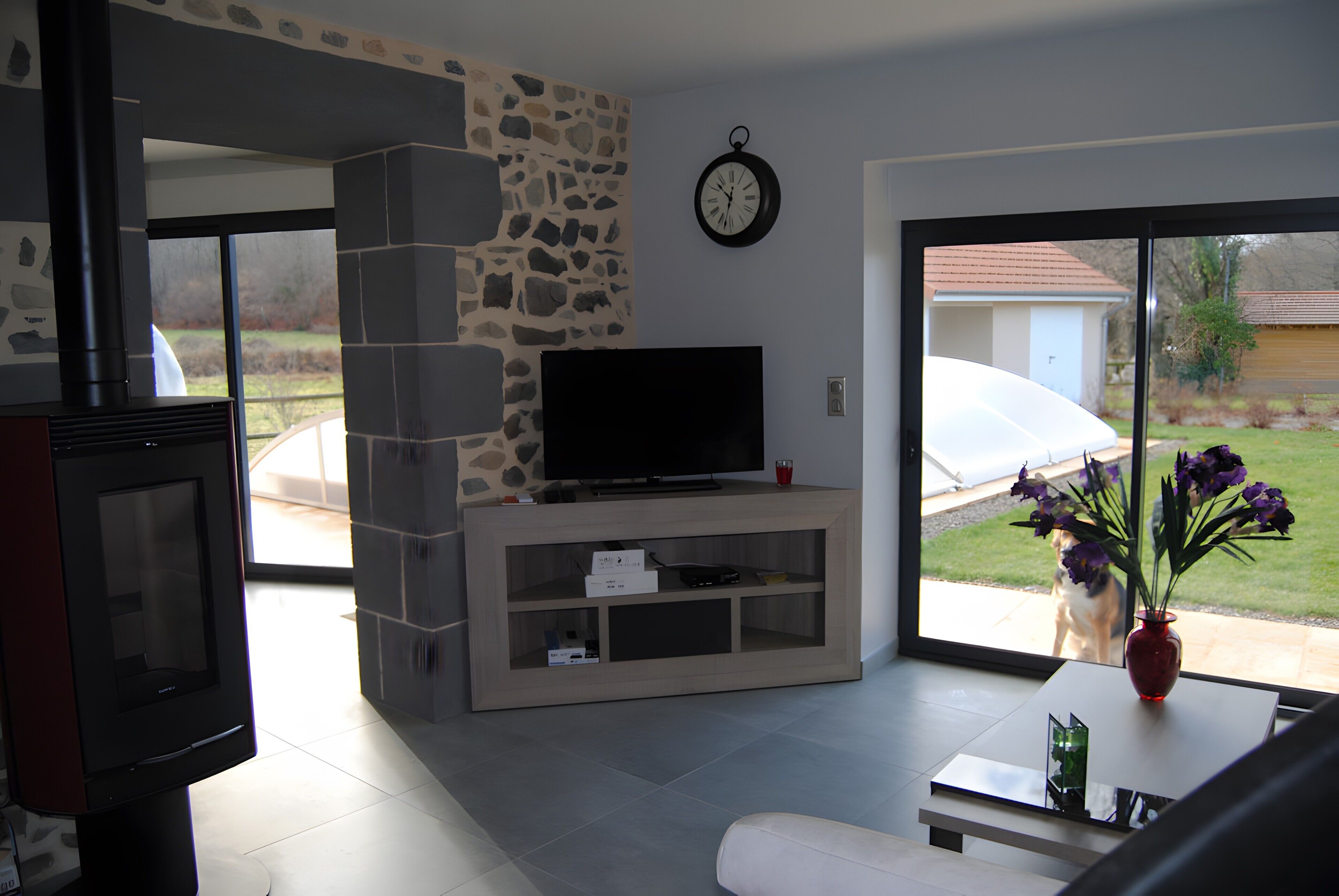 Una sala de estar con chimenea de piedra, un televisor de pantalla plana sobre un mueble de madera y una puerta de cristal que da a un patio.