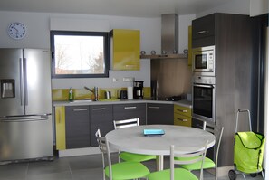 A modern kitchen with a refrigerator, microwave, stove, and a dining table with chairs. - Gîte 'Des Taravelles' with Private Pool, Private Terrace and Wi-Fi (Manzat)