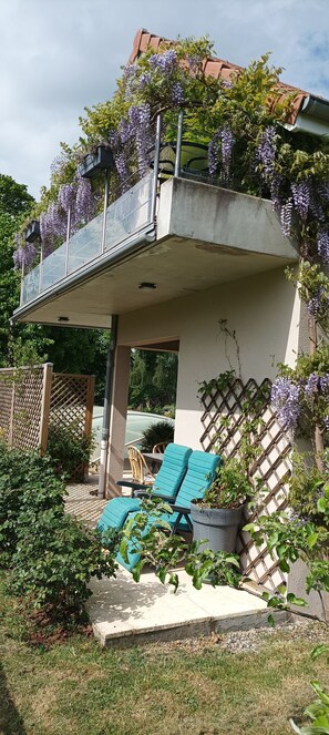 A covered outdoor seating area with a concrete structure, a wooden fence, and purple flowering vines. - Gîte 'Des Taravelles' with Private Pool, Private Terrace and Wi-Fi (Manzat)