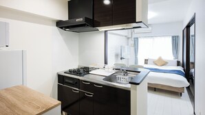 A compact kitchen with a stove, sink, and cabinets, a bed with a view, and a small dining area. -  SPAZIO 2 Canal Hakata (Fukuoka)