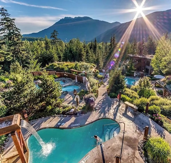 A resort with multiple swimming pools surrounded by lush greenery and mountains in the background.