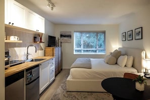 Quarto compacto com cama, mesa de cabeceira e janela com persianas.