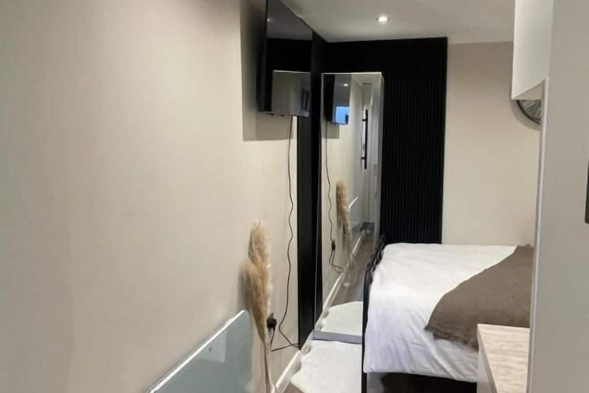 Un dormitorio moderno con una cama, un televisor montado en la pared y un espejo.