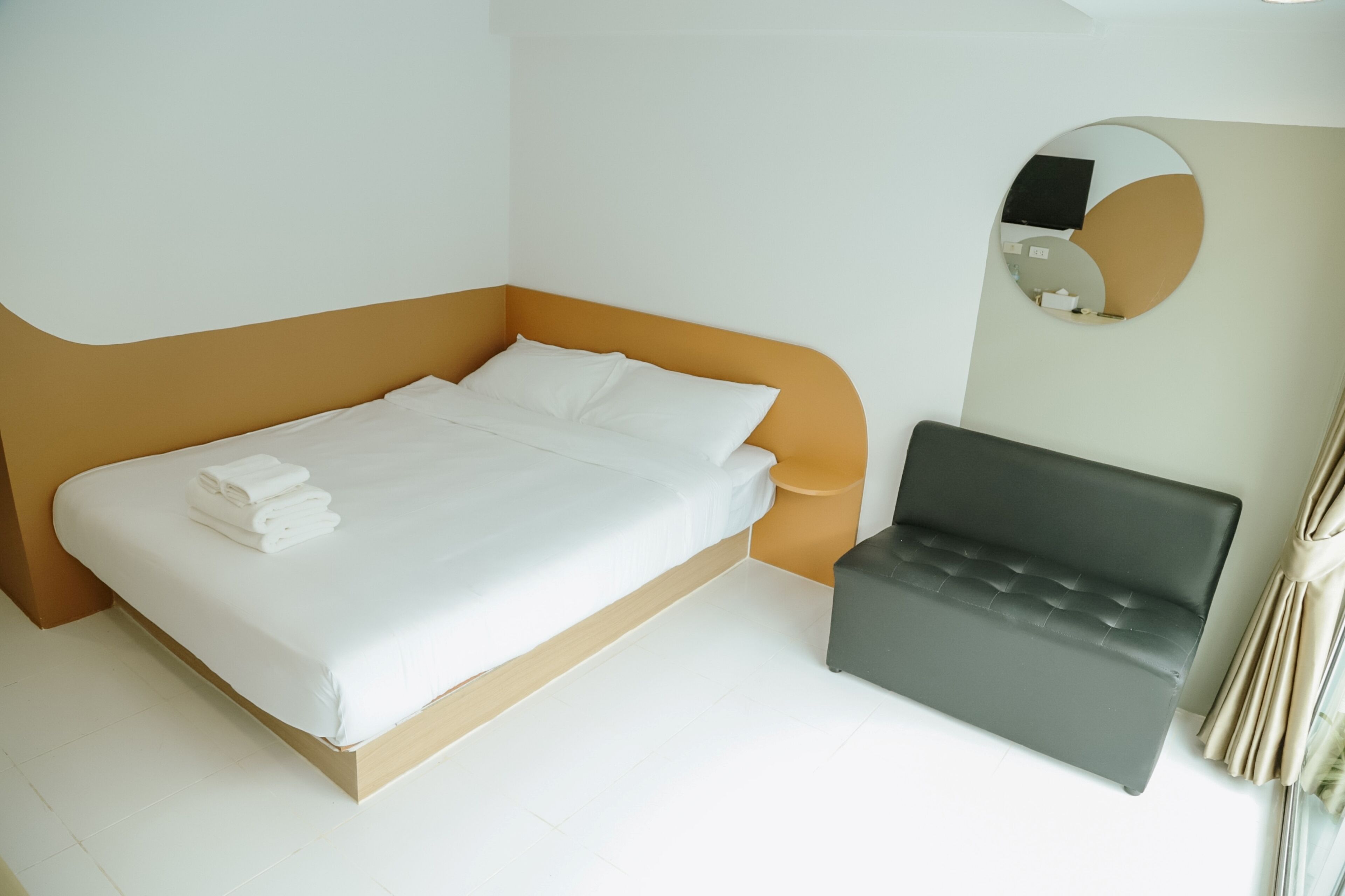 A modern hotel room with a bed, a small sofa, and a round mirror on the wall.