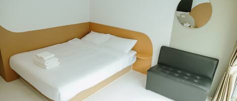 A modern hotel room with a bed, a small sofa, and a round mirror on the wall.