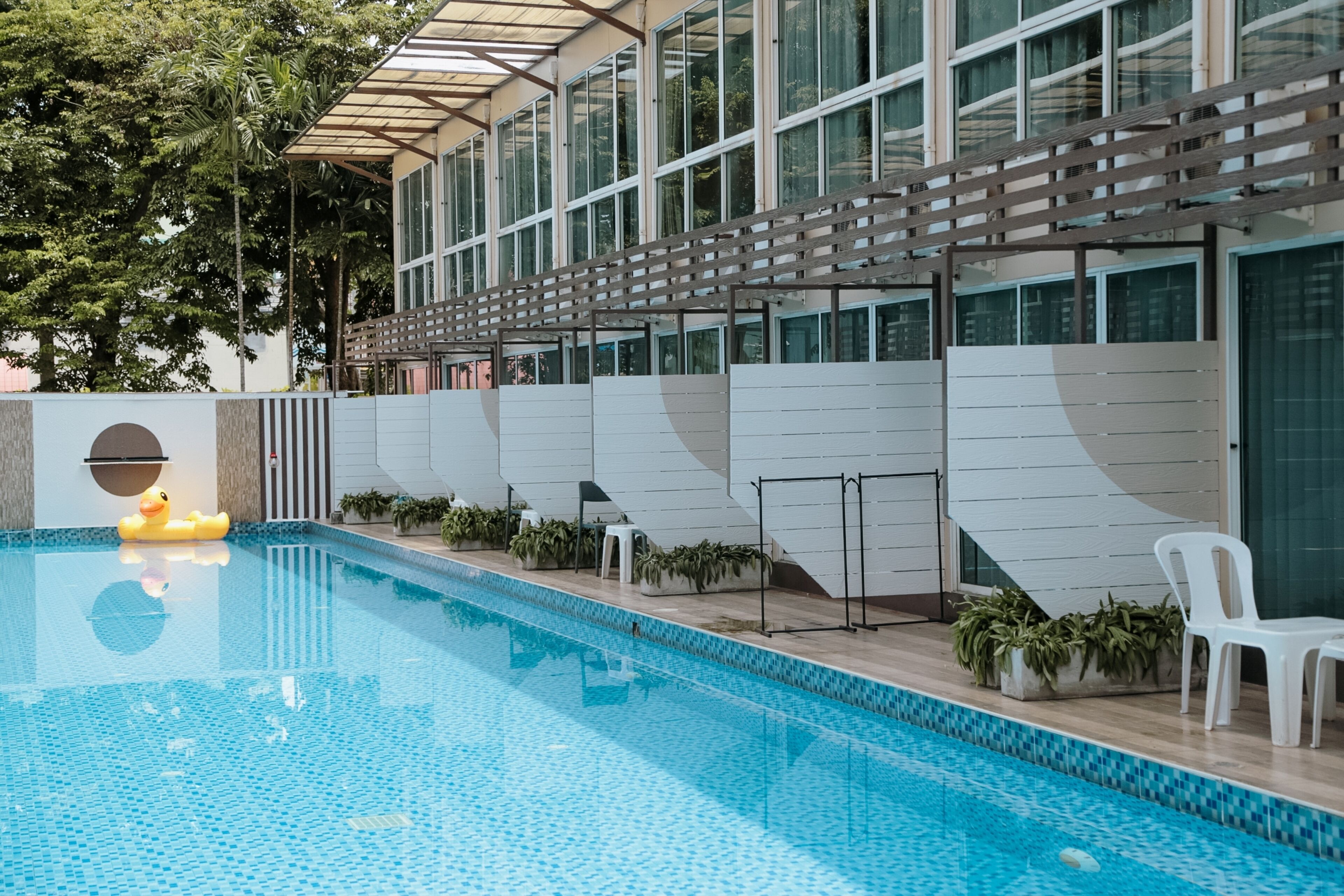 En modern inomhuspool med fri sikt över bassängen, en gul gummianka och en byggnad med stora fönster och en pergola av trä.