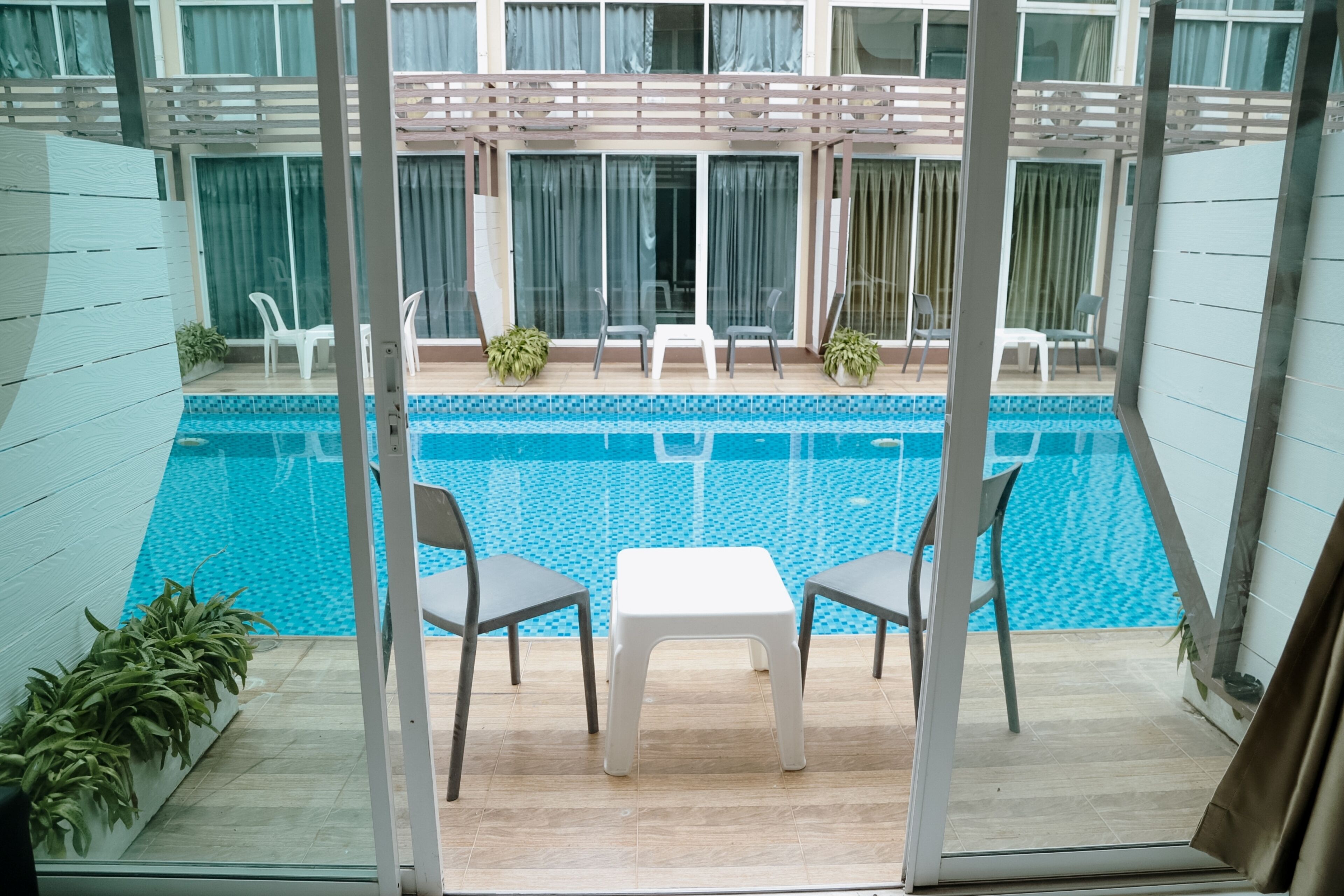 Een zwembadgedeelte met een tafel, stoelen, potplanten en een pergola.