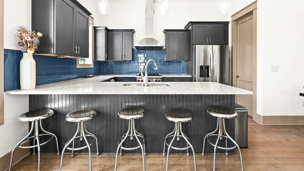 A modern kitchen with dark cabinets, a central island with stools, stainless steel appliances, and pendant lighting.