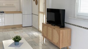 A modern kitchen with white cabinets, a refrigerator, and a dining area with a white table and a potted plant. - Apartment 'Clementina Garden' with Sea View, Wi-Fi and Air Conditioning (Nerja)