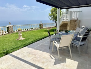 Eine Terrasse mit Tisch und Stühlen, eine Steinmauer, ein weißer Zaun und Blick auf das Meer.