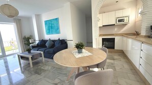 A modern living room with a sofa, a dining table, and a kitchen area with white cabinets and a microwave. - Apartment 'Clementina Garden' with Sea View, Wi-Fi and Air Conditioning (Nerja)
